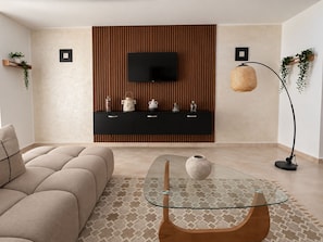 Ein modernes Wohnzimmer mit einer Couch, einem Glastisch, einem an einer Holzwand montierten Fernseher und einer Stehlampe.
