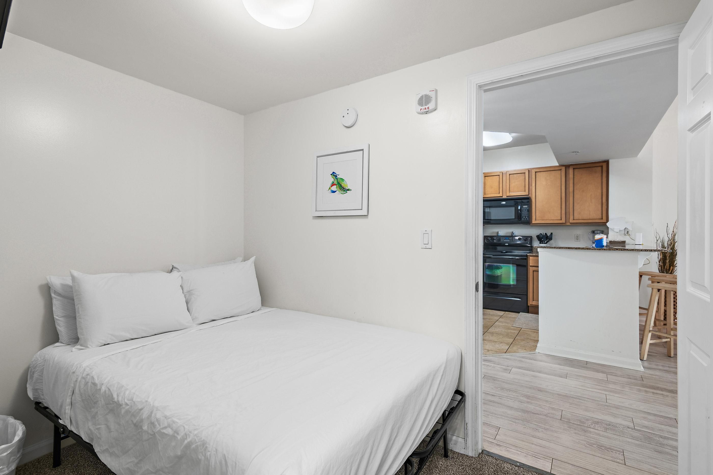 Ein Schlafzimmer mit Bett, einer kleinen Küchenzeile und einem durchgehenden Türspalt sichtbaren Badezimmer.