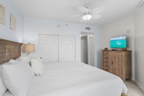 Ein Schlafzimmer mit einem Bett, einem Deckenventilator, einem Fernseher und einer hölzernen Kommode.