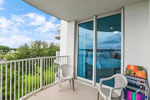 Ein Balkon mit weißer Brüstung, einem weißen Kunststoffstuhl und einem bunten Stuhl mit Ananasmuster.