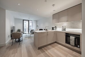 A modern kitchen with built-in appliances, a dining area with a round table and chairs, and a view of the outside balcony. - Elegant One-Bedroom Retreat (London)
