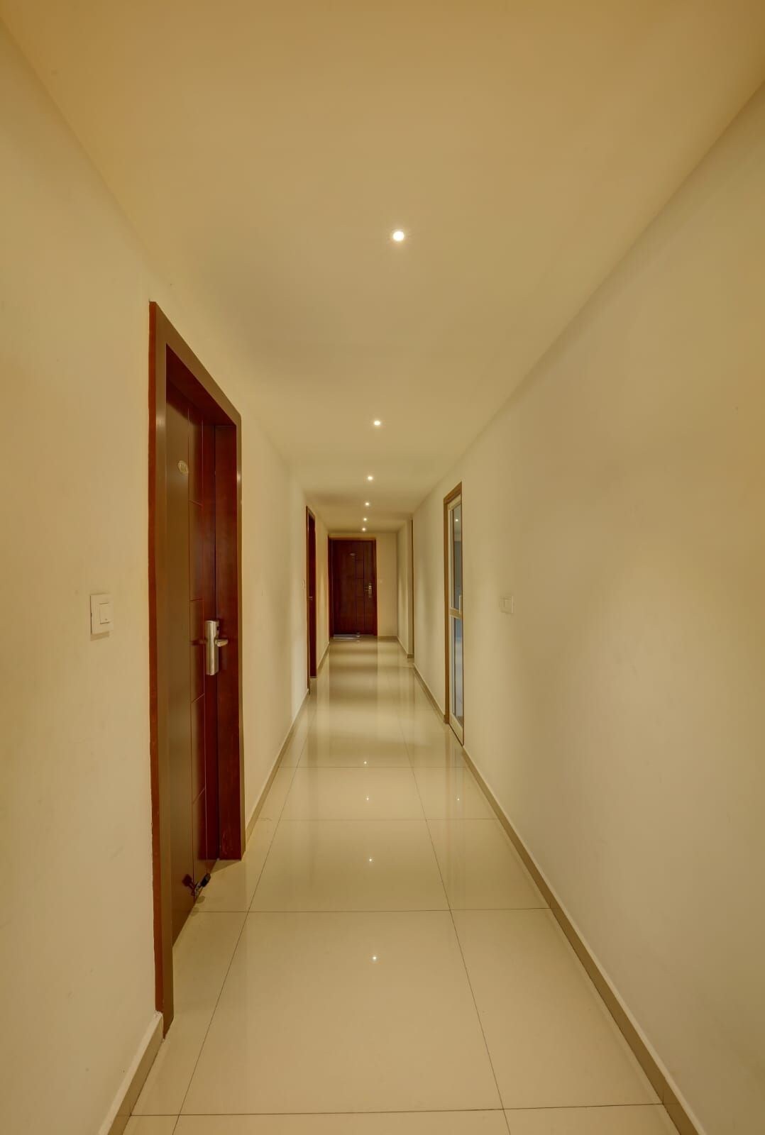 A long, narrow hallway with a wooden door on the left and a window on the right.