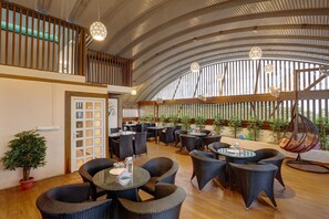 Een ruime binnenruimte met diverse zithoeken, waaronder ronde tafels en stoelen, en een hoog plafond met een gebogen vormgeving.