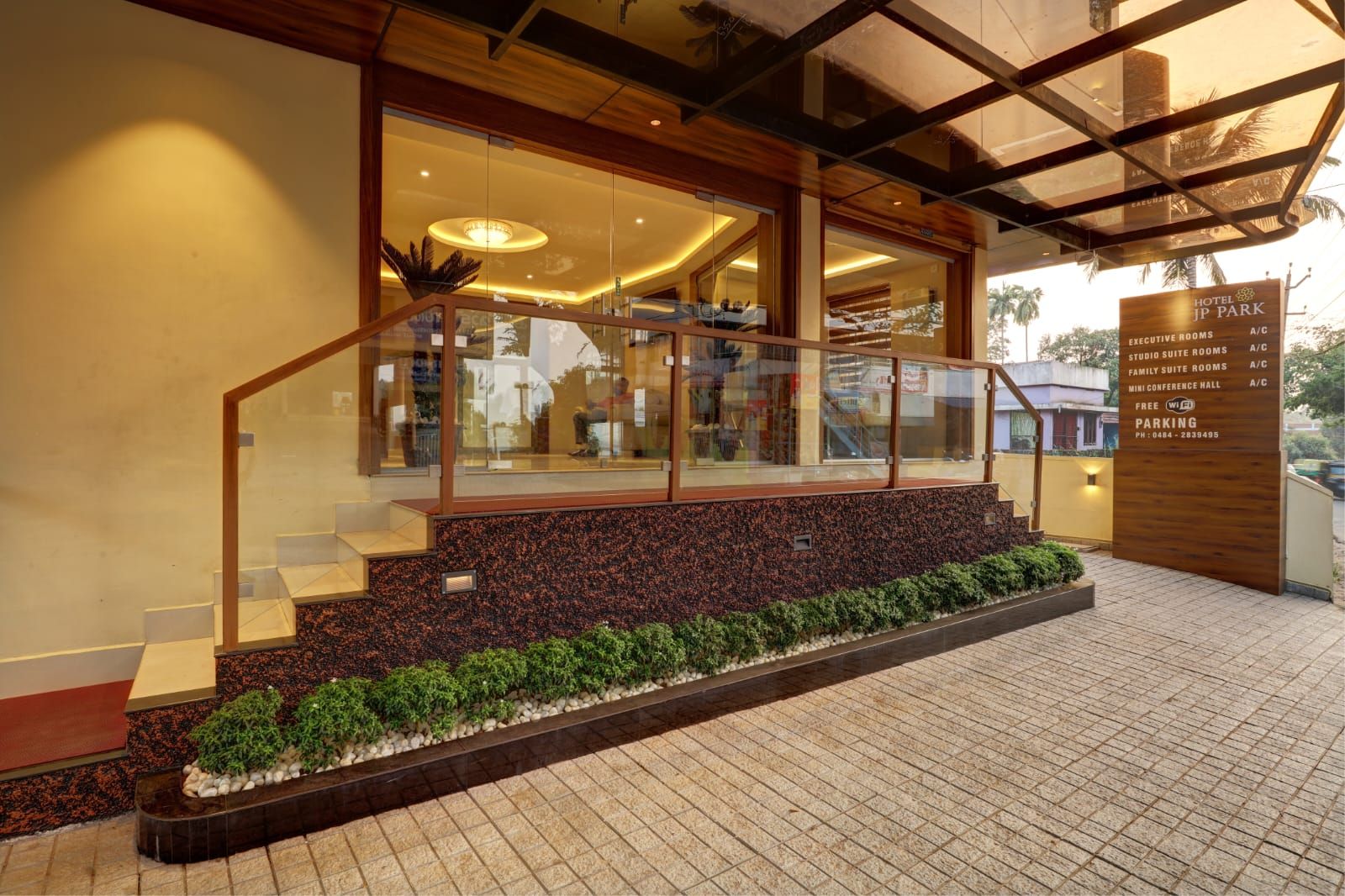 A hotel entrance with a glass staircase, a reception desk, and a sign indicating executive rooms, studio suite rooms, family suite rooms, and a mini conference hall.