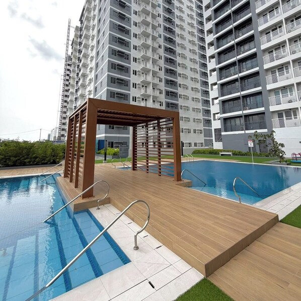 Ein Schwimmbecken mit Holzterrasse und Metallgeländern, umgeben von einem Hochhauswohnhaus.