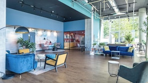 A modern lounge area with seating, a reception desk, and a large window providing natural light. - Light-Filled Living - One Bedroom Apartment, Sleeps 2 (Salford)