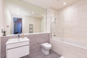 A modern bathroom with a glass-enclosed shower, a white toilet, and a vanity with a mirror. - Light-Filled Living - One Bedroom Apartment, Sleeps 2 (Salford)