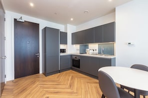 A modern kitchen with grey cabinets, a wooden herringbone floor, a built-in oven, and a dining area with a white table and chairs.