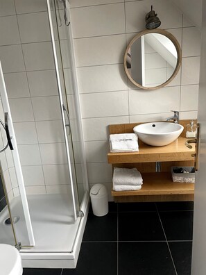 Une salle de bain avec une douche à parois de verre, un lavabo blanc avec un meuble-vasque en bois et un miroir au-dessus du lavabo.
