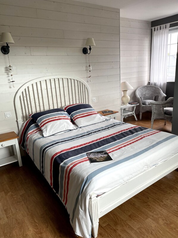 Un lit avec une couvre-lit à rayures, deux lampes fixées au mur, une chaise et une petite table avec une lampe.