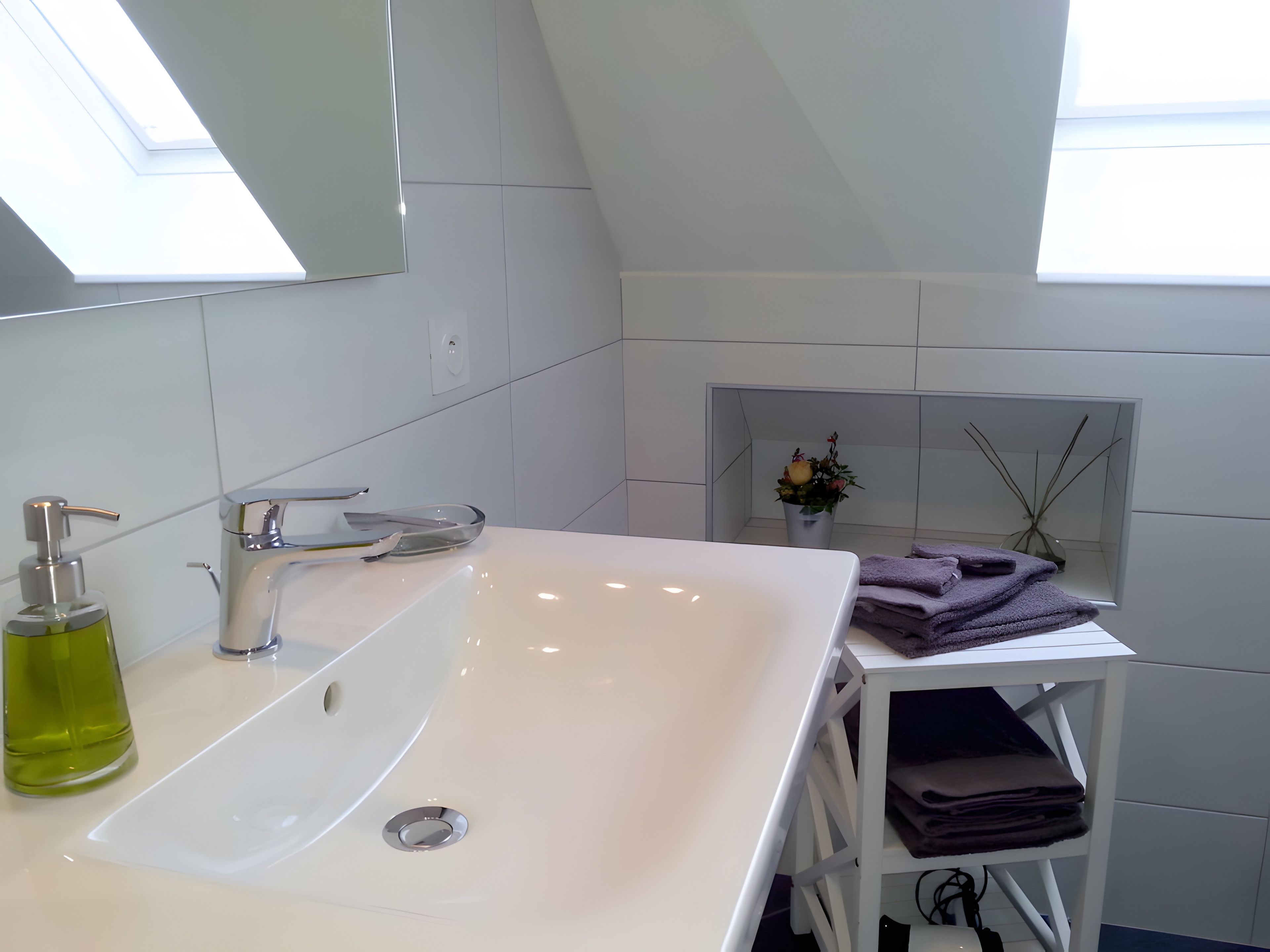 Un baño moderno con un lavamanos blanco, un espejo y un tragaluz.