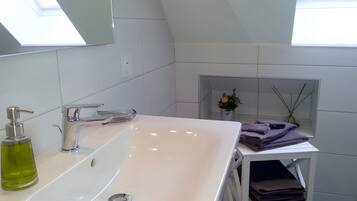 Un baño moderno con un lavamanos blanco, un espejo y un tragaluz.