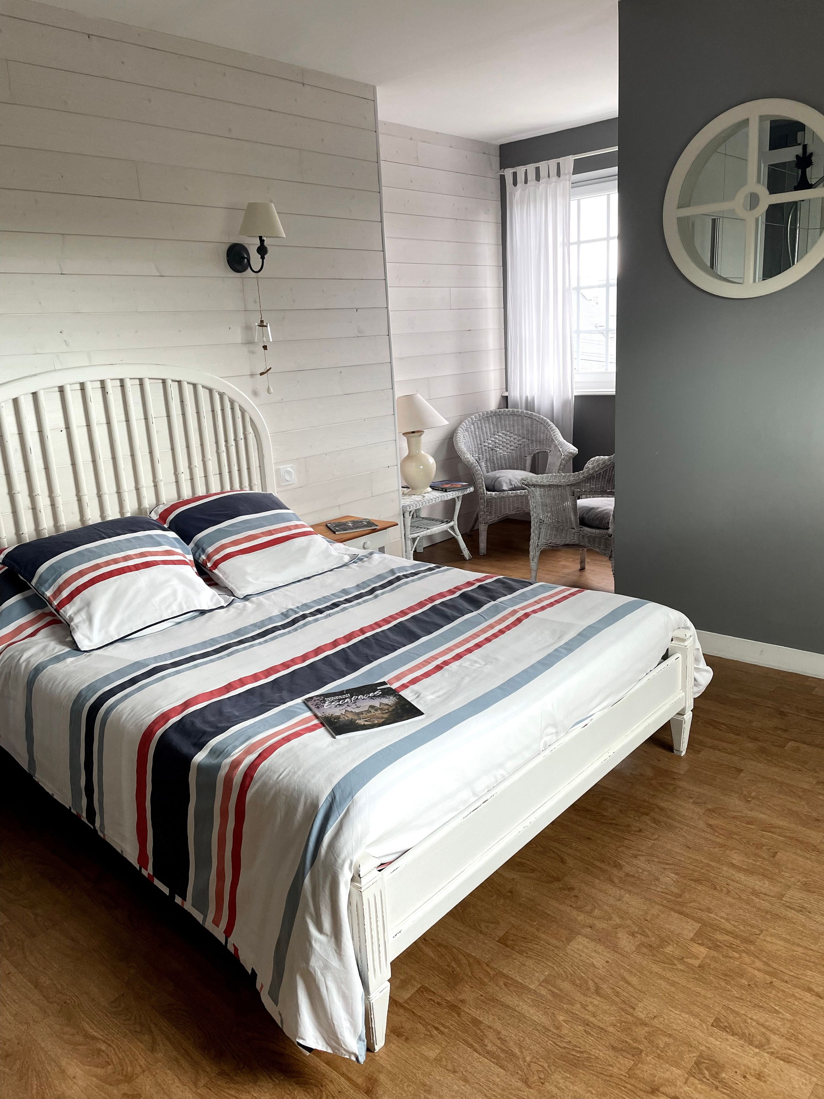 Un dormitorio con cama, una silla, una lámpara y un espejo montado en la pared.