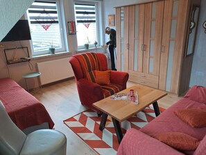 Uma sala de estar com sofá, poltrona, mesa de madeira e um armário.