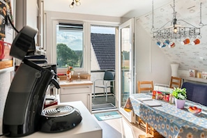 A kitchen with a coffee machine, a dining area with a table and chairs, and a view through the window.