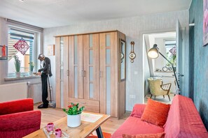 A modern living room with a wooden wardrobe, red sofas, a wooden coffee table with a plant, and a dining area with a chair and table. - Apartment 'Fewo-basche' with Balcony and Wi-Fi (Barsinghausen)
