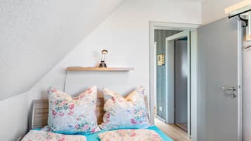 A bedroom with a bed, pillows, a nightstand, a wall-mounted lamp, and a door.
