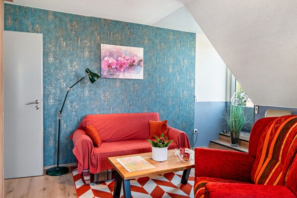 A cozy room with a red sofa, a small table with a map, a floor lamp, and a wall with a blue textured design.