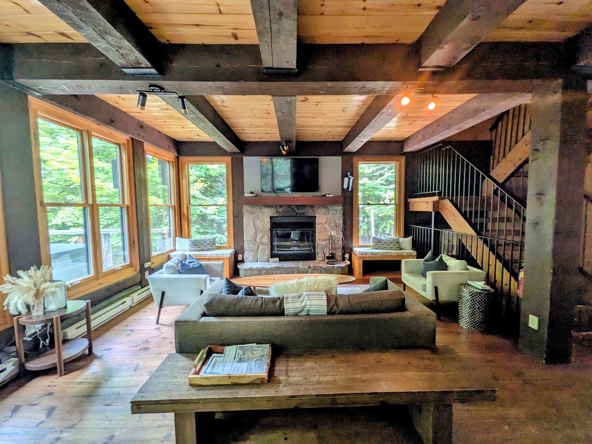 A spacious living room with a fireplace, large windows, and a staircase.