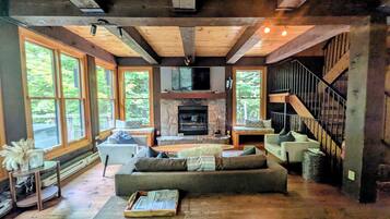 A spacious living room with a fireplace, large windows, and a staircase.