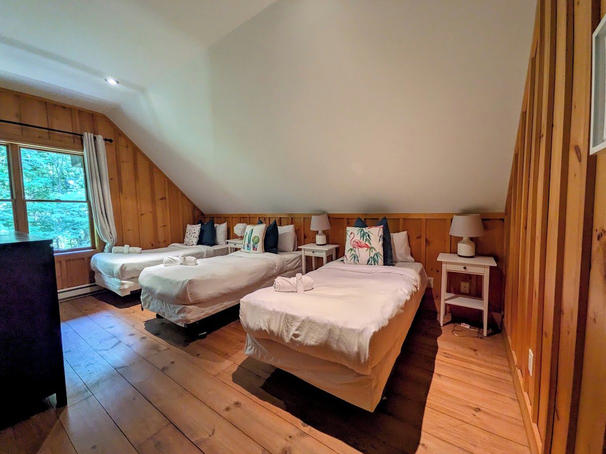 Une chambre avec deux lits, un plancher en bois, une fenêtre avec des rideaux et une petite table avec une lampe.
