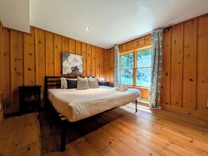 Un dormitorio con una cama grande, paredes de madera, una ventana con cortinas y un cuadro en la pared.