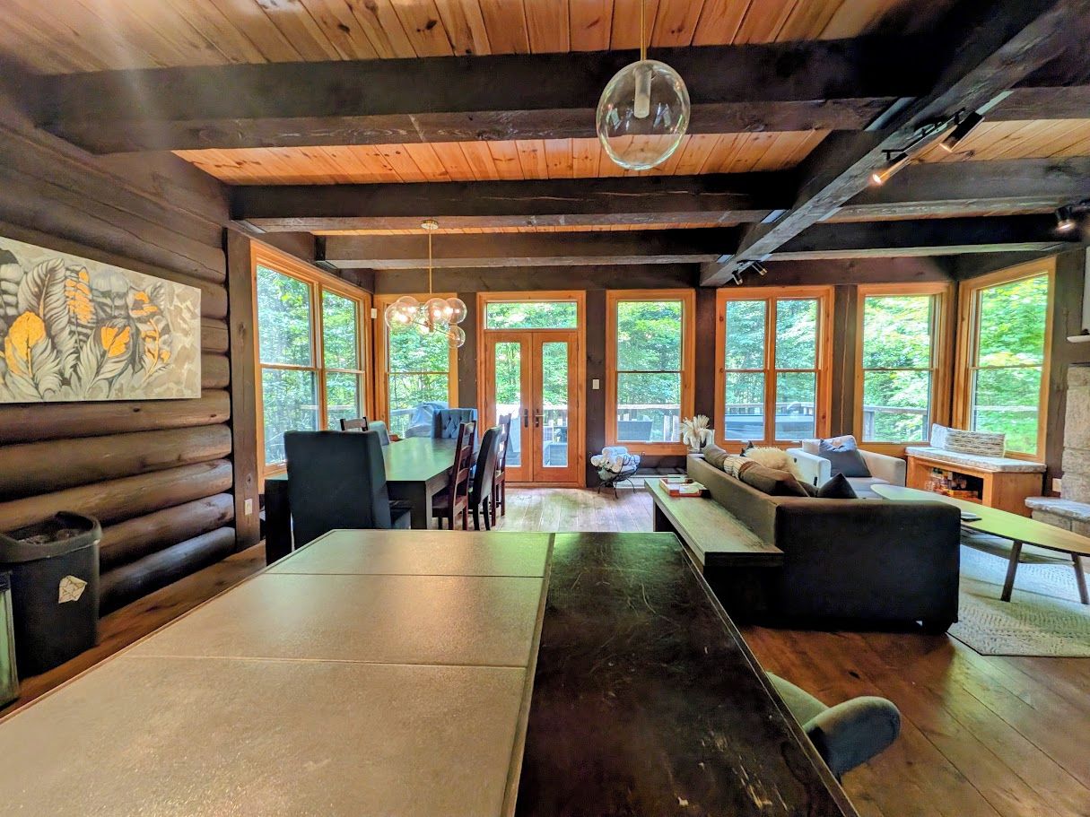 L’intérieur d’une cabane en rondins comprend une table à manger, des chaises, un canapé et une grande fenêtre donnant sur le paysage extérieur.