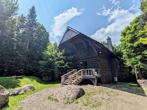 A log cabin with a wooden staircase leading to a porch, surrounded by trees and rocks. - Luxurious Cozy Getaway with great skiing, outdoor activities, hot tub, EVR. (Lac-Supérieur)