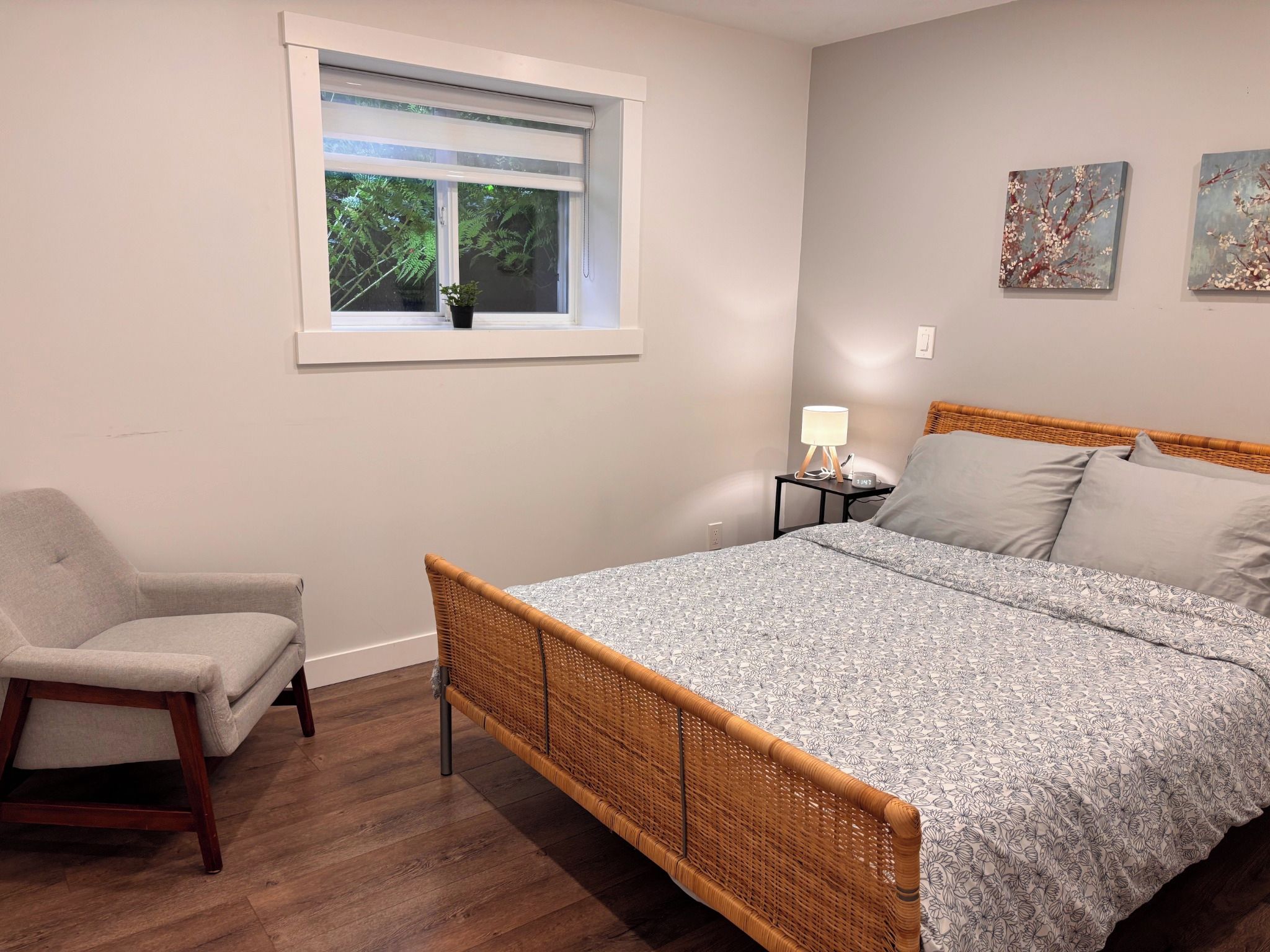 Une chambre à coucher comprenant un lit, une chaise, une table de chevet avec une lampe et une fenêtre donnant sur un paysage verdoyant.