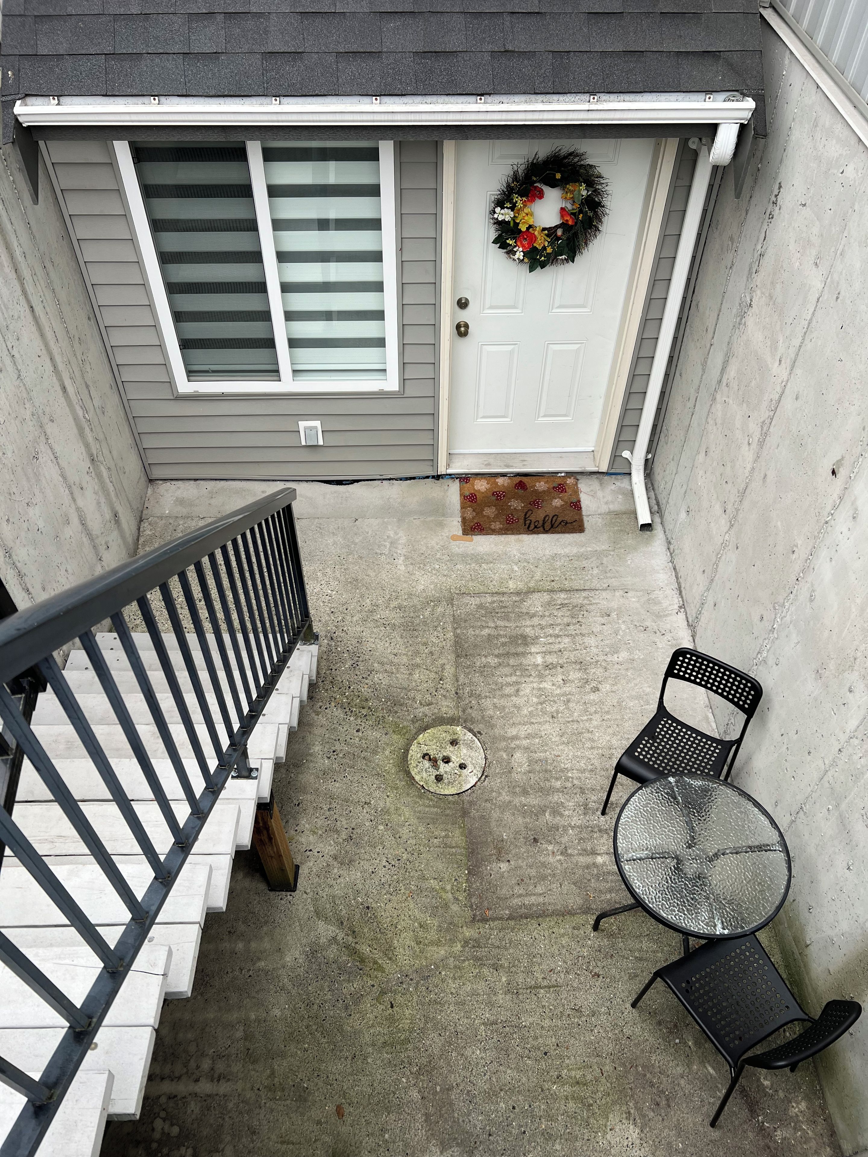 A residential exterior with a front door, a mailbox, a concrete step, a metal chair, and a small table.