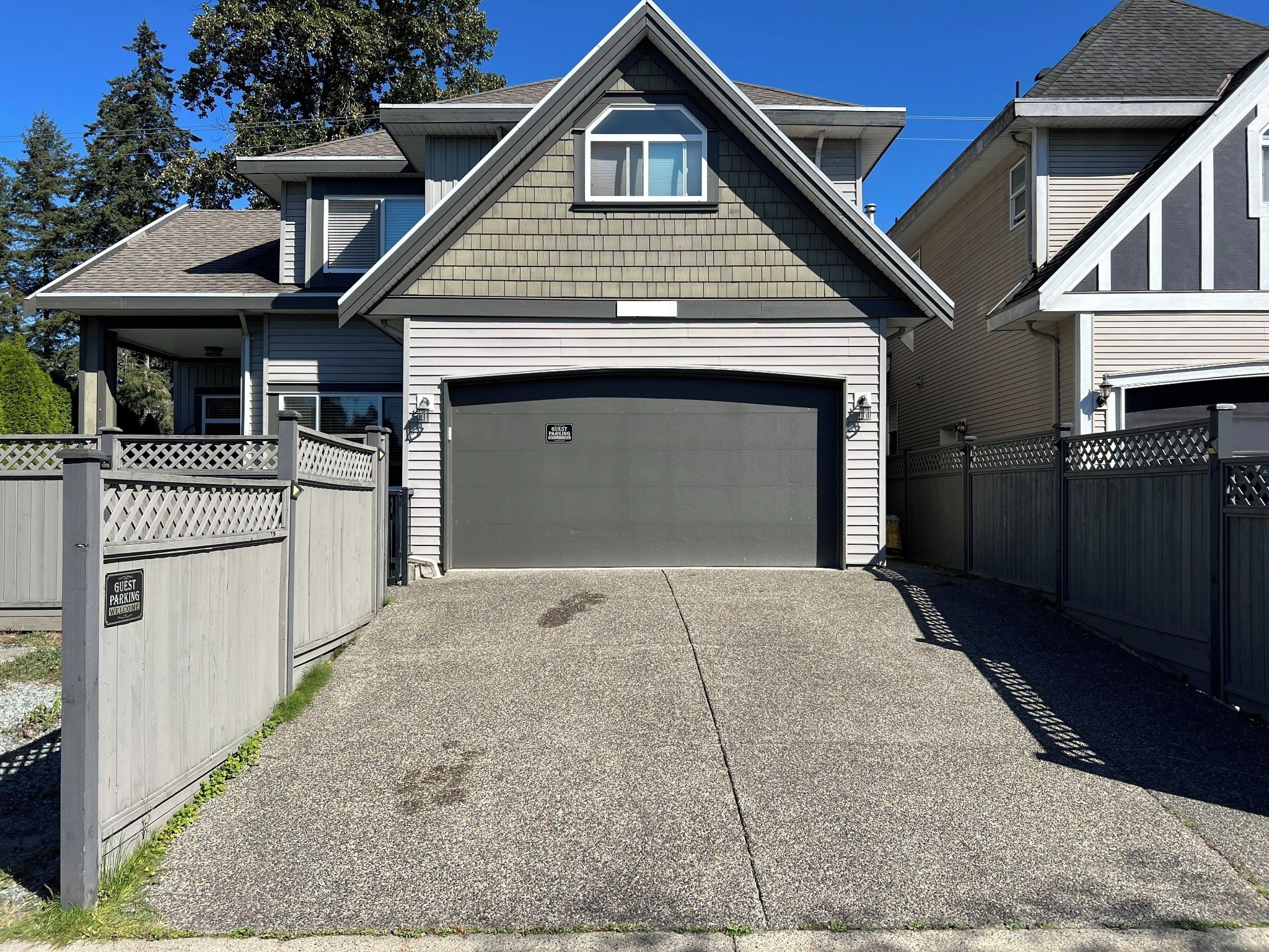 Une maison à deux étages avec un garage, une véranda et une allée gravillonnée.