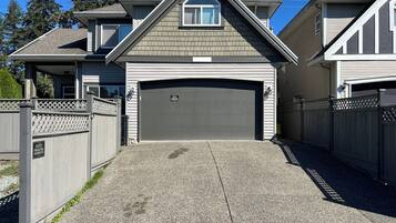 Une maison à deux étages avec un garage, une véranda et une allée gravillonnée.