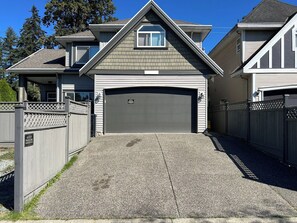 Une maison à deux étages avec un garage, une véranda et une allée gravillonnée.