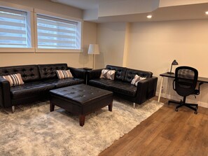 Un salon comprenant deux canapés en cuir noir, un pouf assorti, un bureau en bois avec une chaise et une lampe.