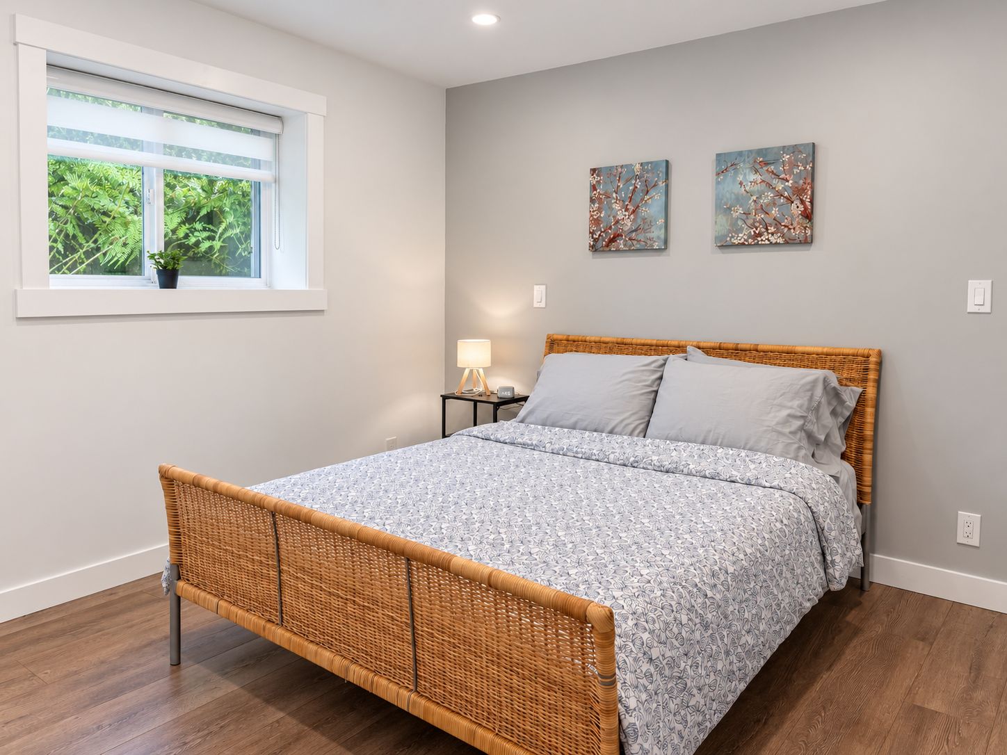 A bedroom with a bed, a window with a view of greenery, and two wall-mounted paintings.