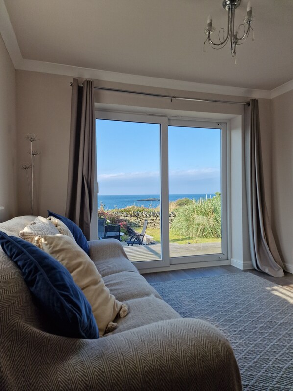 A bedroom with a large sliding glass door leading to a balcony with a view of the sea.