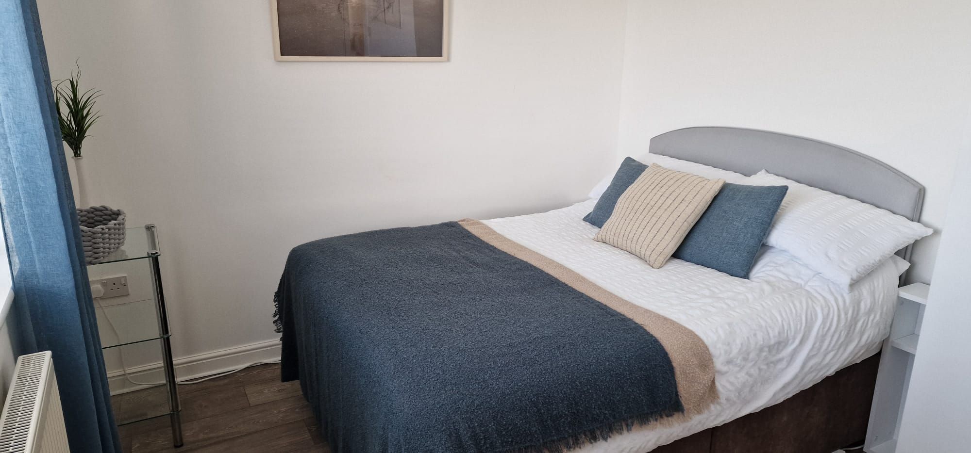 Una cama bien hecha con un cabecero gris, una colcha azul y varios almohadones en tonos azules y blancos.