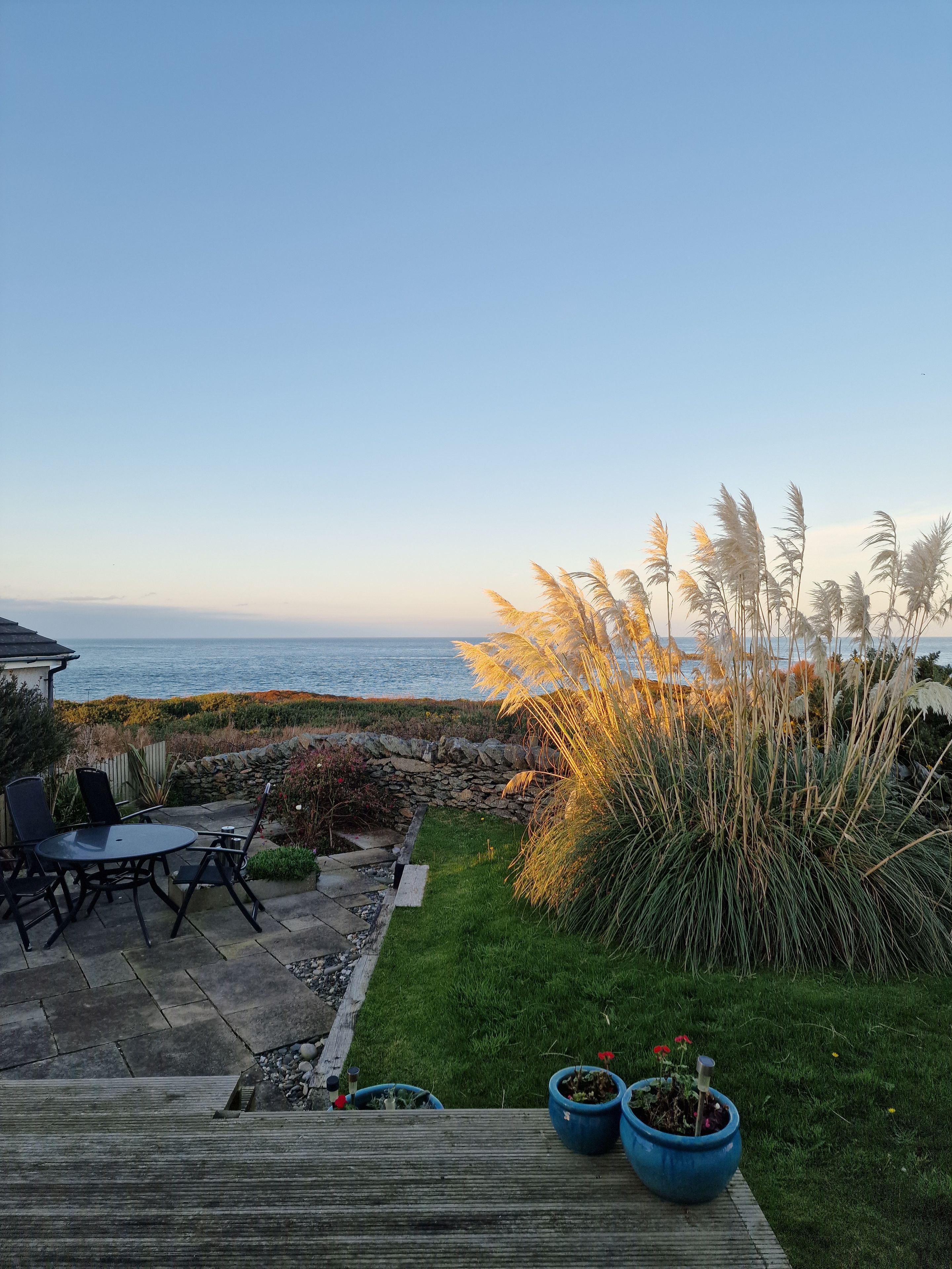 A patio with a table and chairs, a stone wall, and a view of the sea.