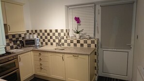 A compact kitchen with a microwave, sink, and cabinets. - Seaside Bungalow with Wide Reaching Views (Amlwch)