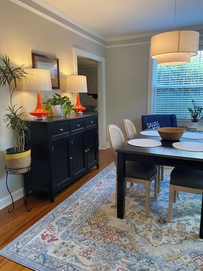 A dining area with a black table, white chairs, a patterned rug, and a black cabinet with two orange lamps. - Cozy 1-bedroom Cottage-In-The-Trees!. (Tallahassee)