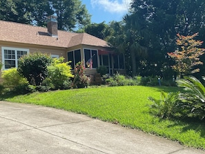 A residential house with a well-maintained lawn, a covered porch, and a flag. - Cozy 1-bedroom Cottage-In-The-Trees!. (Tallahassee)