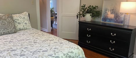 A bedroom with a bed, a dresser, a plant, and a lamp.