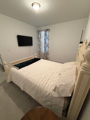 A bedroom with a bed, a television mounted on the wall, and a window with curtains. - Welcoming 1-bedroom house with AC in charming Littleton (Littleton)