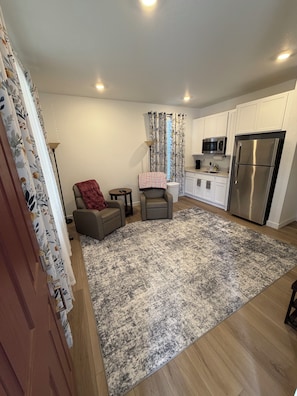 A compact living space with a kitchenette, a grey sofa, a patterned rug, and a red throw blanket. - Welcoming 1-bedroom house with AC in charming Littleton (Littleton)