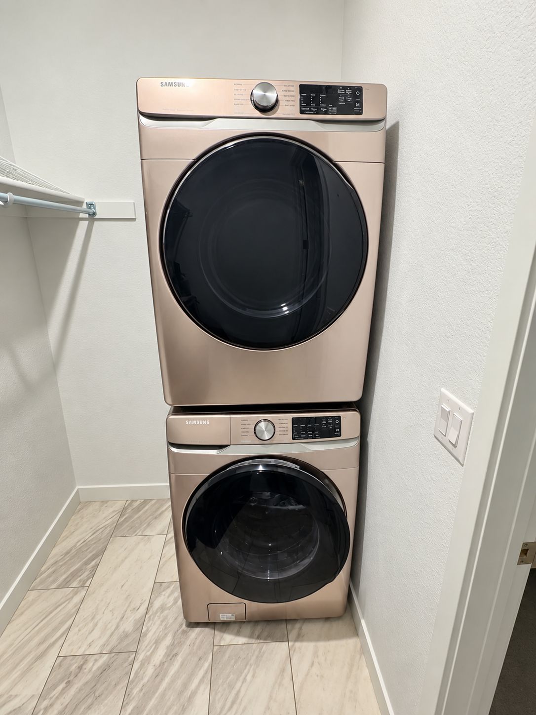 Un appareil combiné lave-linge et sèche-linge fixé au mur, placé dans un coin, avec un revêtement de sol de couleur claire.