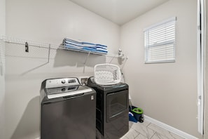 A laundry area with a washing machine, dryer, and a shelf with folded towels. - Sleeps 15·Private Pool·Themed Rooms·Game Room (Kissimmee)