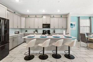 A modern kitchen with white cabinets, a central island with bar stools, a refrigerator, and a microwave. - Sleeps 15·Private Pool·Themed Rooms·Game Room (Kissimmee)