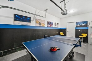 A ping pong table with a projector and seating in a room with artwork on the walls. - Sleeps 15·Private Pool·Themed Rooms·Game Room (Kissimmee)