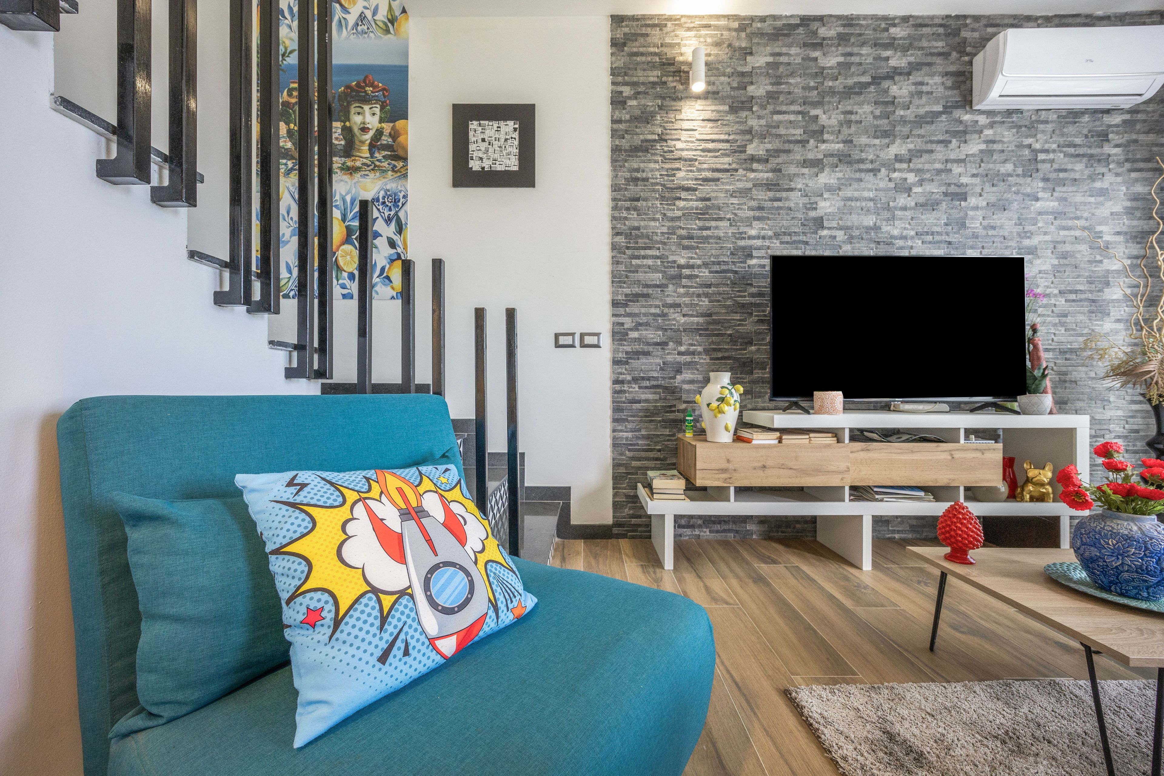 A modern living room with a teal sofa, a flat-screen TV, and a stone wall.