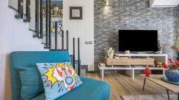 A modern living room with a teal sofa, a flat-screen TV, and a stone wall.